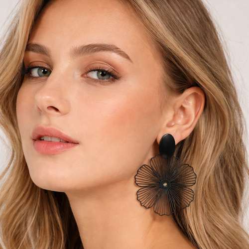Woman wearing black floral earrings with a plain background