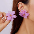Close-up of a person wearing pink floral earrings with a hand holding one.