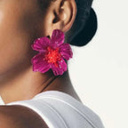 Close-up of a person wearing a vibrant pink flower earring with a red center.